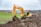Close-up of a yellow mini excavator bucket digging soil in a residential garden.