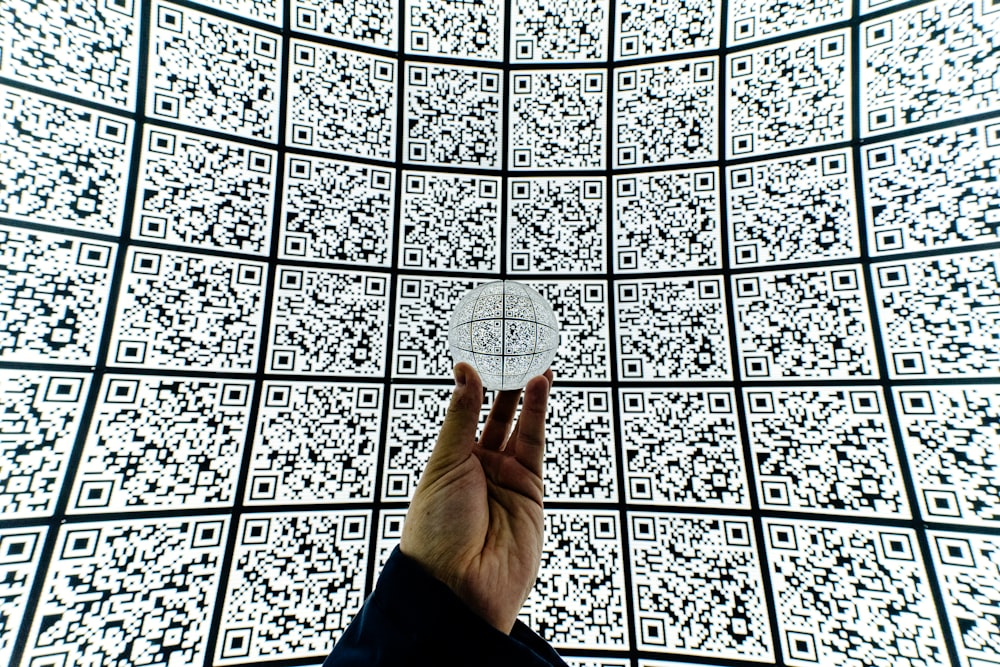persona sosteniendo una bola de vidrio transparente con fondo de código QR