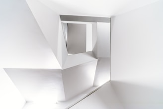 A modern architectural interior with clean, geometric lines and sharp angles in a monochromatic color scheme. The structure features an arrangement of triangular and rectangular shapes creating an abstract and minimalist design.