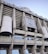 Tall structural facade of a large stadium with visible columns and a silver-gray exterior. The signage reads 'Estadio Santiago Bernabéu' and there is a prominent logo of Real Madrid Club de Fútbol displayed.