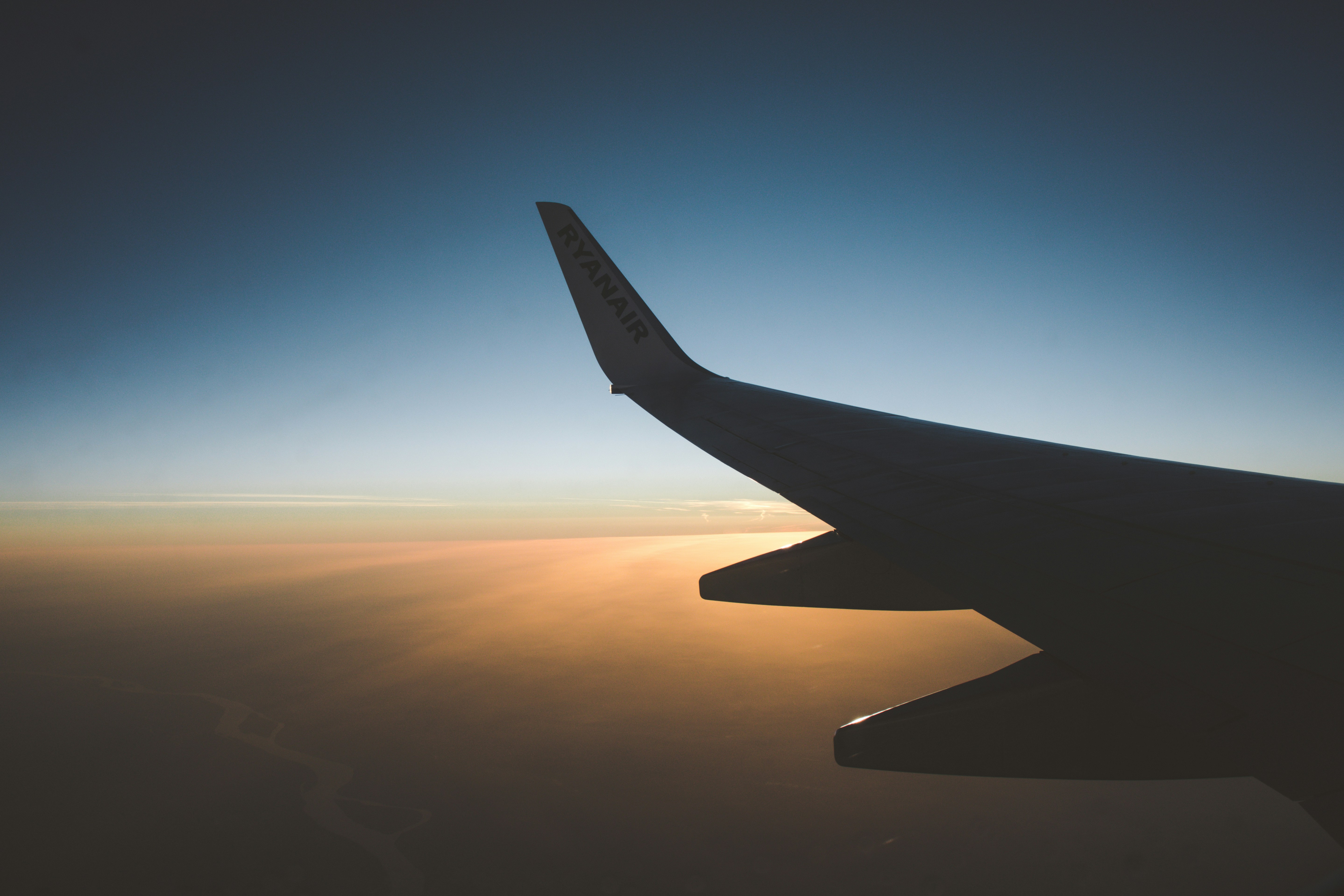 photo of airplane wing taken inside the plane above the clouds during sunrise, 