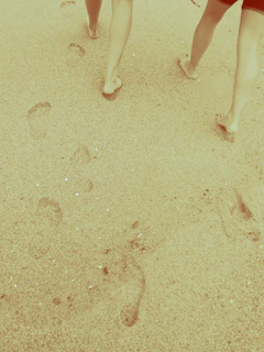 Smiling travelers walking barefoot along a sandy shore with footprints behind them.
