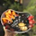 Close-up of a hand holding a vibrant, hand-thrown stoneware bowl with fresh fruit inside.