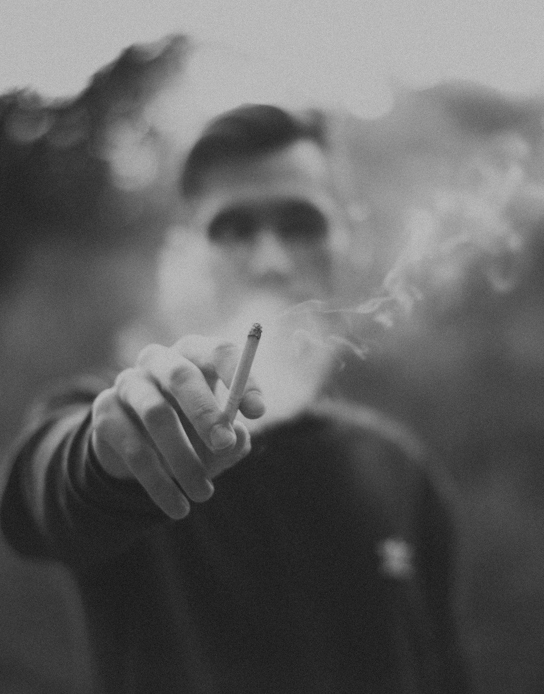 grayscale and selective focus photography of man holding single cigarette stick
