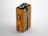 A close-up view of a rectangular 9V battery with an orange and black design. The battery is labeled 'Industrial by Duracell' and 'Professional Alkaline Battery.' Various icons and text, including production details and recycling information, are printed on the surface.