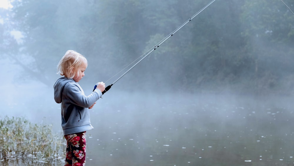 釣り竿を保持している灰色のパーカーを着た幼児