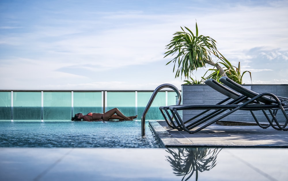 femme couchée à la piscine à côté de la clôture pendant la journée