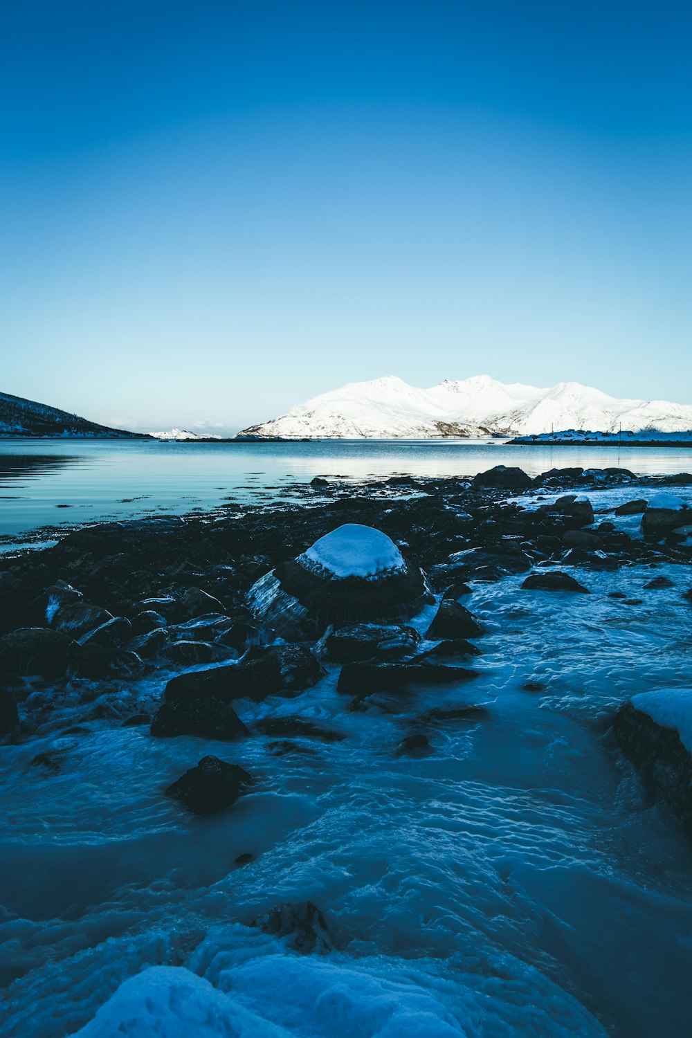 mountain covered with snow near calm body of water during daytime