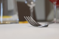 Close-up of a sleek stainless steel fork resting on a glass plate with a soft linen napkin.