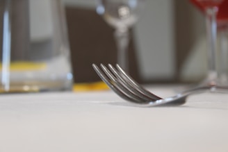 Close-up of a sleek stainless steel fork resting on a glass plate with a soft linen napkin.
