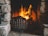 A warm and inviting fireplace with a bright, roaring fire, surrounded by a rustic stone setting. A black teapot is placed on the left side of the hearth, adding a cozy touch to the scene.