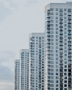 A series of modern high-rise apartment buildings with numerous windows and balconies, positioned side by side in a slightly staggered formation. The buildings appear to be well-maintained and have a uniform architectural style with a clean, minimalistic design.