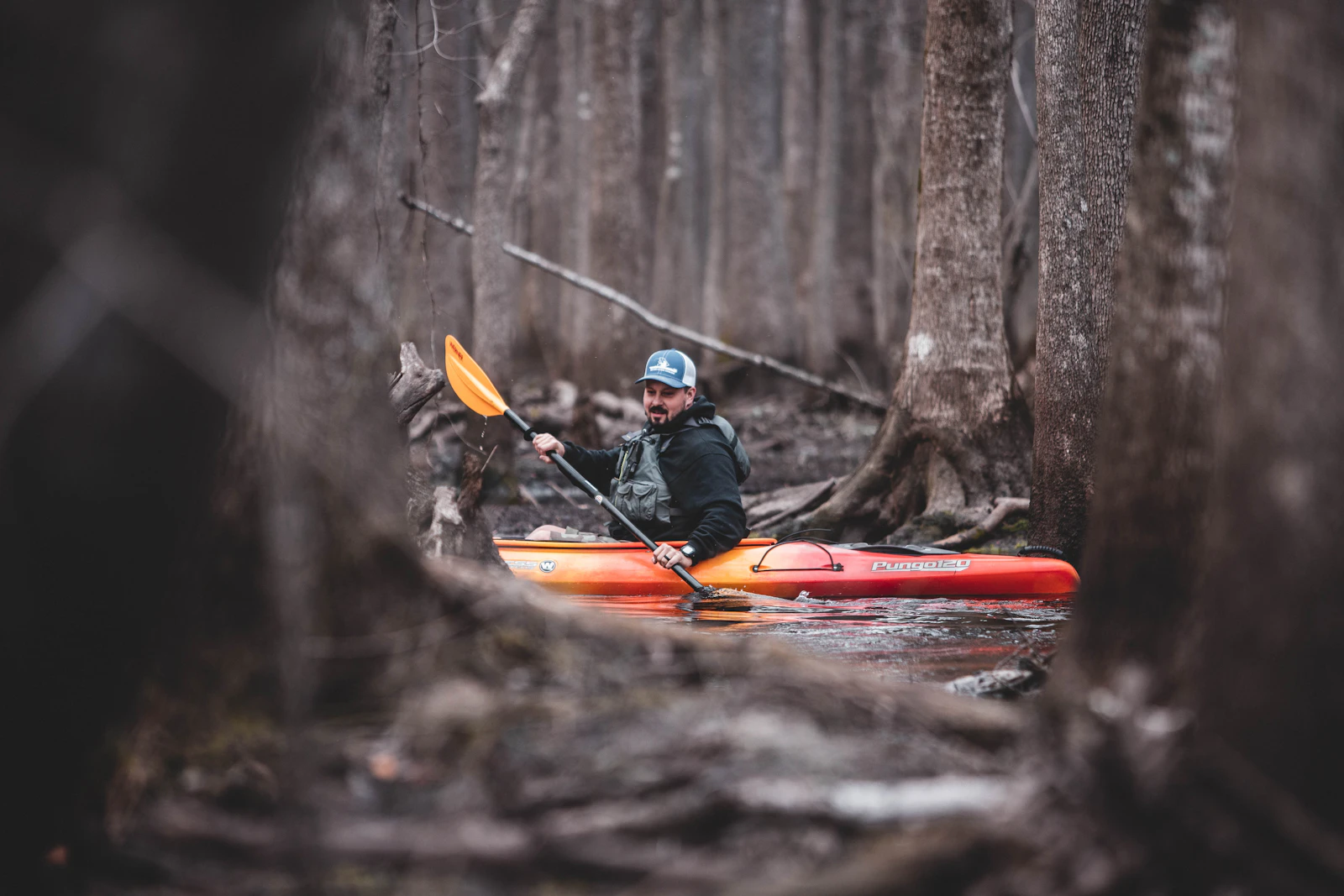 Kayak rouge descendant une rivière en eau vive entre des rochers, style descente de la Lesse