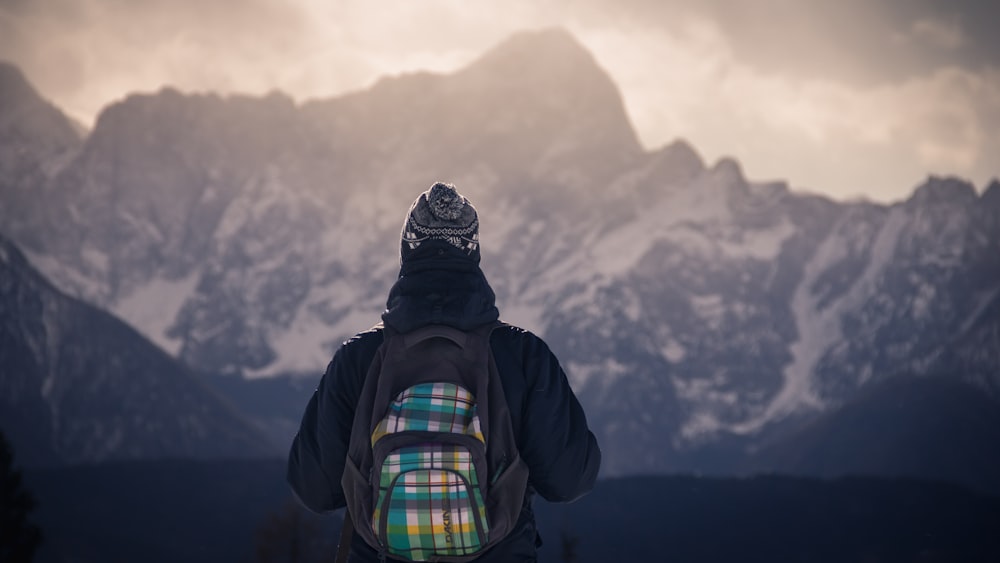 Person, die tagsüber einen Rucksack trägt und vor einem schneebedeckten Berg steht