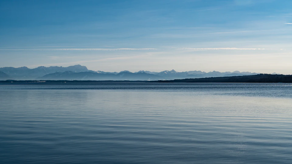 Serene lake surrounded by majestic mountains under a clear blue sky with wispy clouds