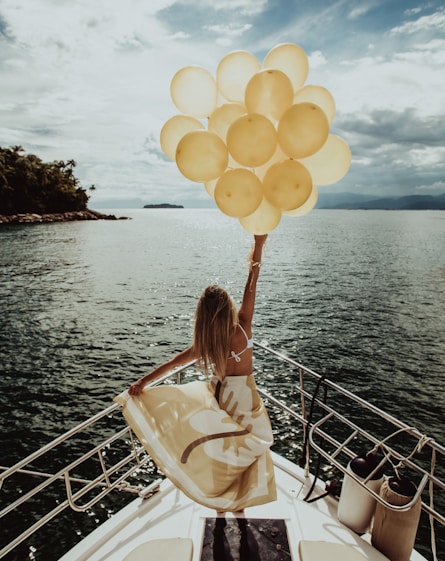woman holding gold balloons while standing on a yacht