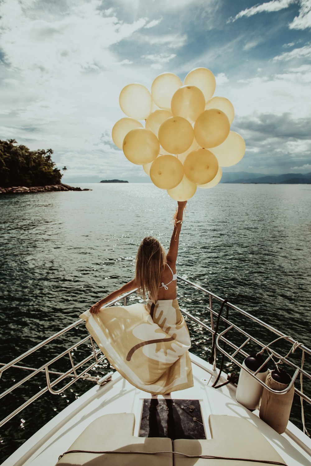 Frau hält goldene Luftballons, während sie auf einer Yacht steht