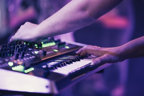 Close-up of a musician's hands playing a synthesizer with purple neon lights reflecting.