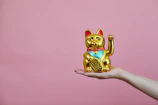 A close-up of a golden maneki-neko brocade accessory glowing softly against a dark navy background with subtle asanoha patterns.