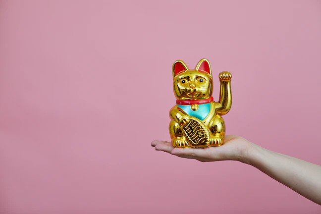 A close-up of a golden maneki-neko brocade accessory glowing softly against a dark navy background with subtle asanoha patterns.