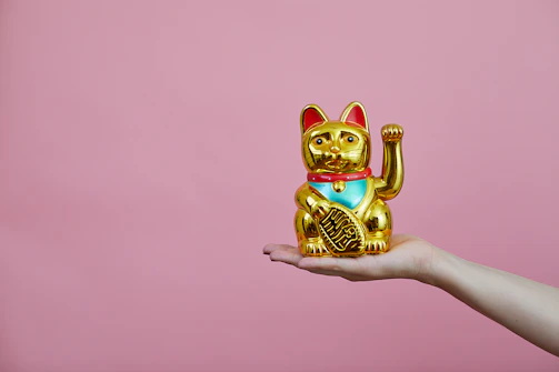 A golden Maneki-neko cat statue glowing softly against a dark navy background with subtle Japanese hemp leaf patterns.