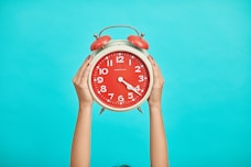 person holding red and beige twin bell analog alarm clock