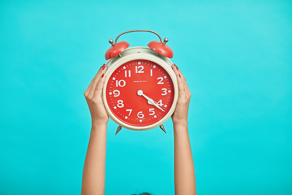 Hands holding a red alarm clock against a blue background, highlighting the importance of time management.