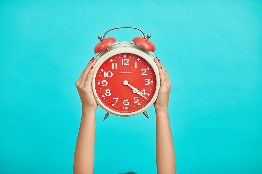 person holding red and beige twin bell analog alarm clock