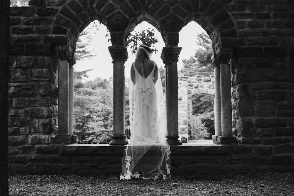 grayscale photography of woman standing between arch and pillar