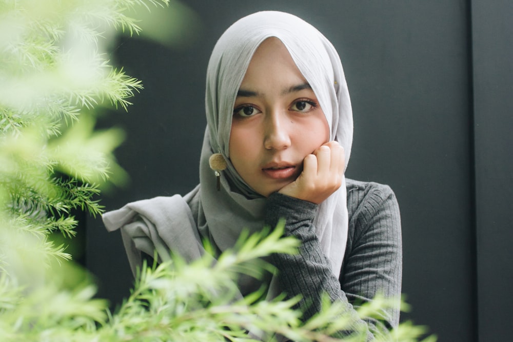 woman wearing gray long-sleeved top and gray hijab right hand on cheek