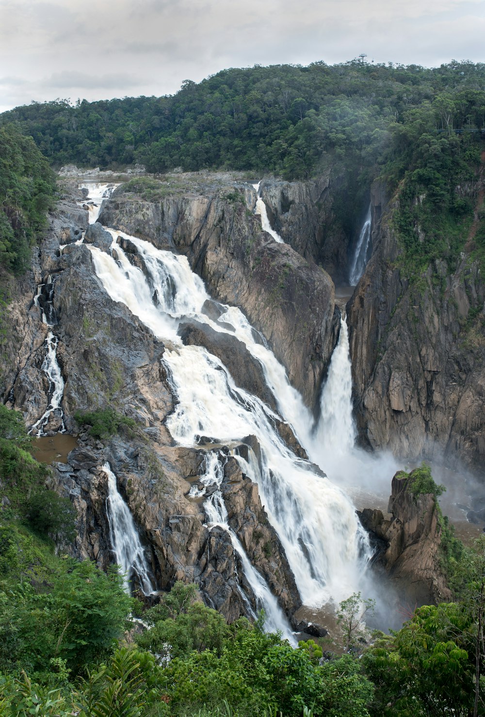 waterfalls lined with trees under grey cloudy sky