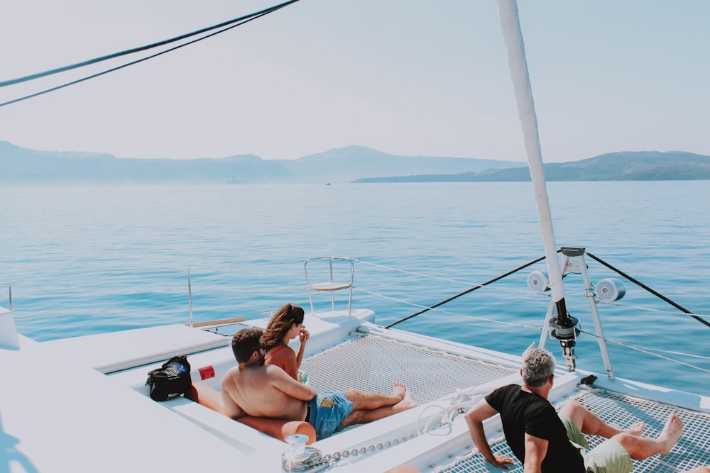 three person sitting on white yacht viewing calm sea