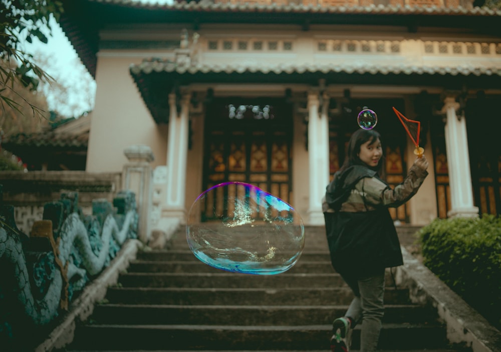 woman in grey jacket walking on stairs making soapy bubbles