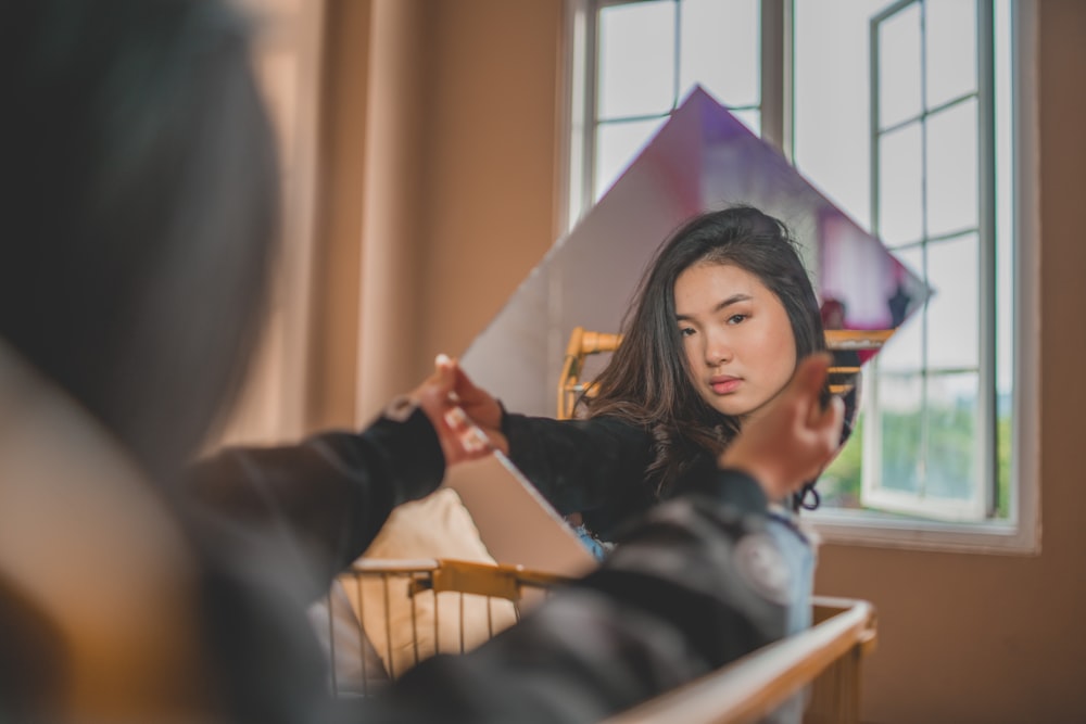 femme en veste noire se reflétant sur le miroir tout en tenant avec les deux mains