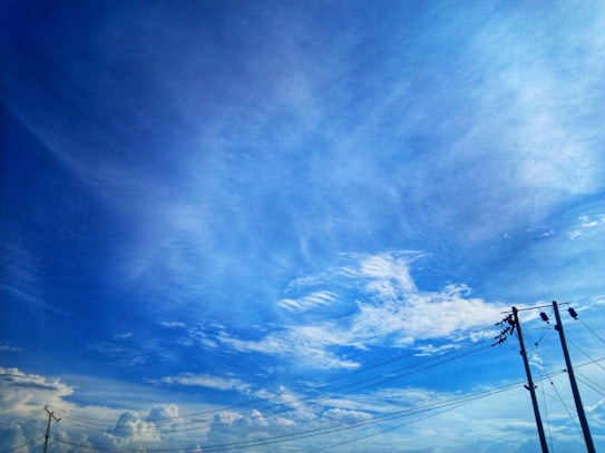 A clear blue sky with some scattered white clouds. There are utility poles and power lines visible, extending across the right side of the image.