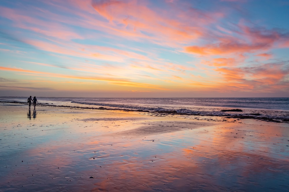 two person walking on shore during golden hour