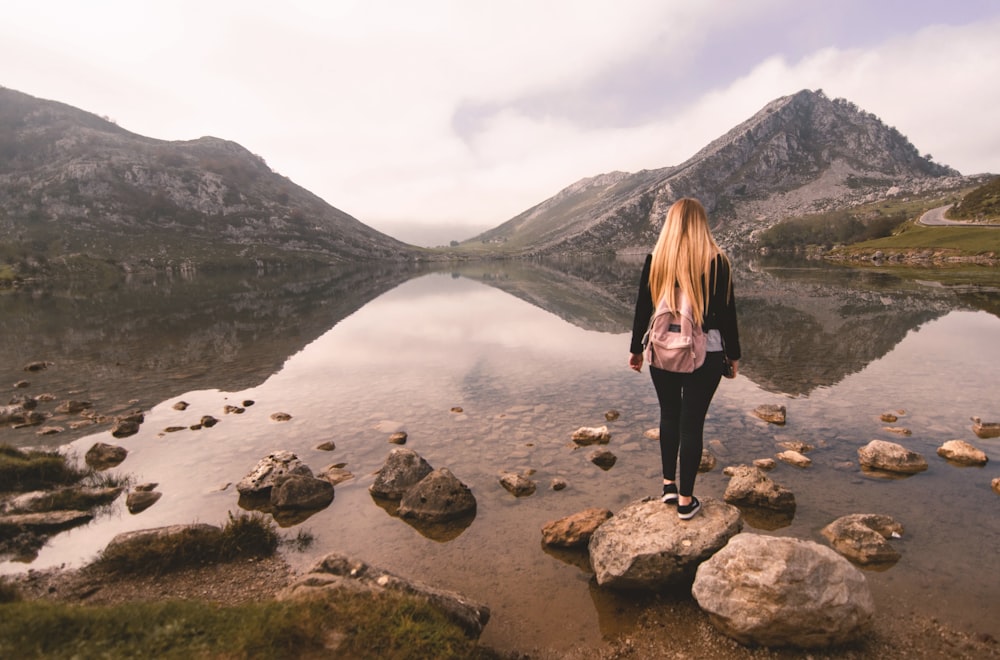 Mujer de pie en la parte superior de la roca en el cuerpo de agua durante el día