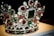 A luxurious crown adorned with an array of precious gemstones and pearls. The design features large red and green stones surrounded by a multitude of smaller clear crystals, creating an intricate and opulent pattern.