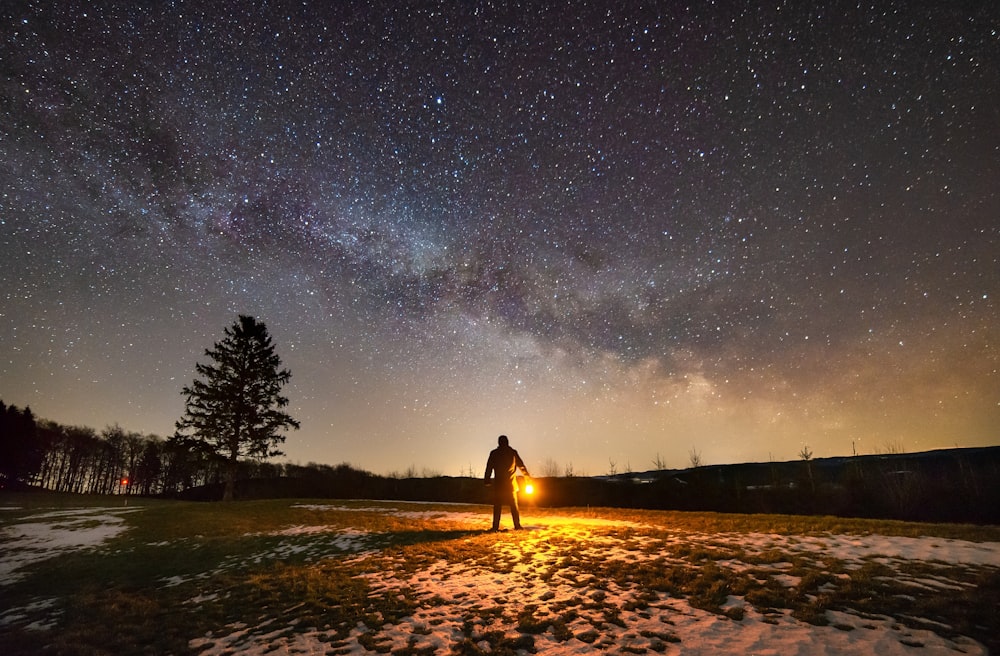 person holding torch in middle of open field under starry sky