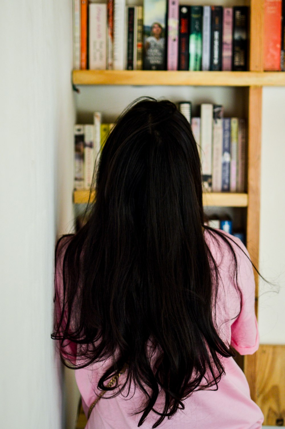 woman leaning on wall looking at bookshelf