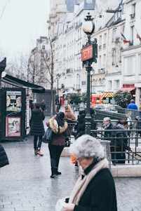 A bustling street scene showing colorful shops, people enjoying outdoor dining, and the nearby metro station entrance.