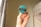 A hand holding a round badge with a teal background and a black stripe in the center. On the stripe, the text 'MISCELLANY 4.5 2017-2020' is printed in white. The background consists of light-colored curtains with a minimal pattern and a partial view of a white bed with draped fabric.