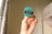 A hand holding a round badge with a teal background and a black stripe in the center. On the stripe, the text 'MISCELLANY 4.5 2017-2020' is printed in white. The background consists of light-colored curtains with a minimal pattern and a partial view of a white bed with draped fabric.
