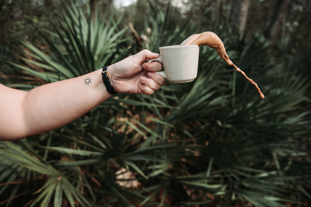 person holding white ceramic teacup spilling coffee