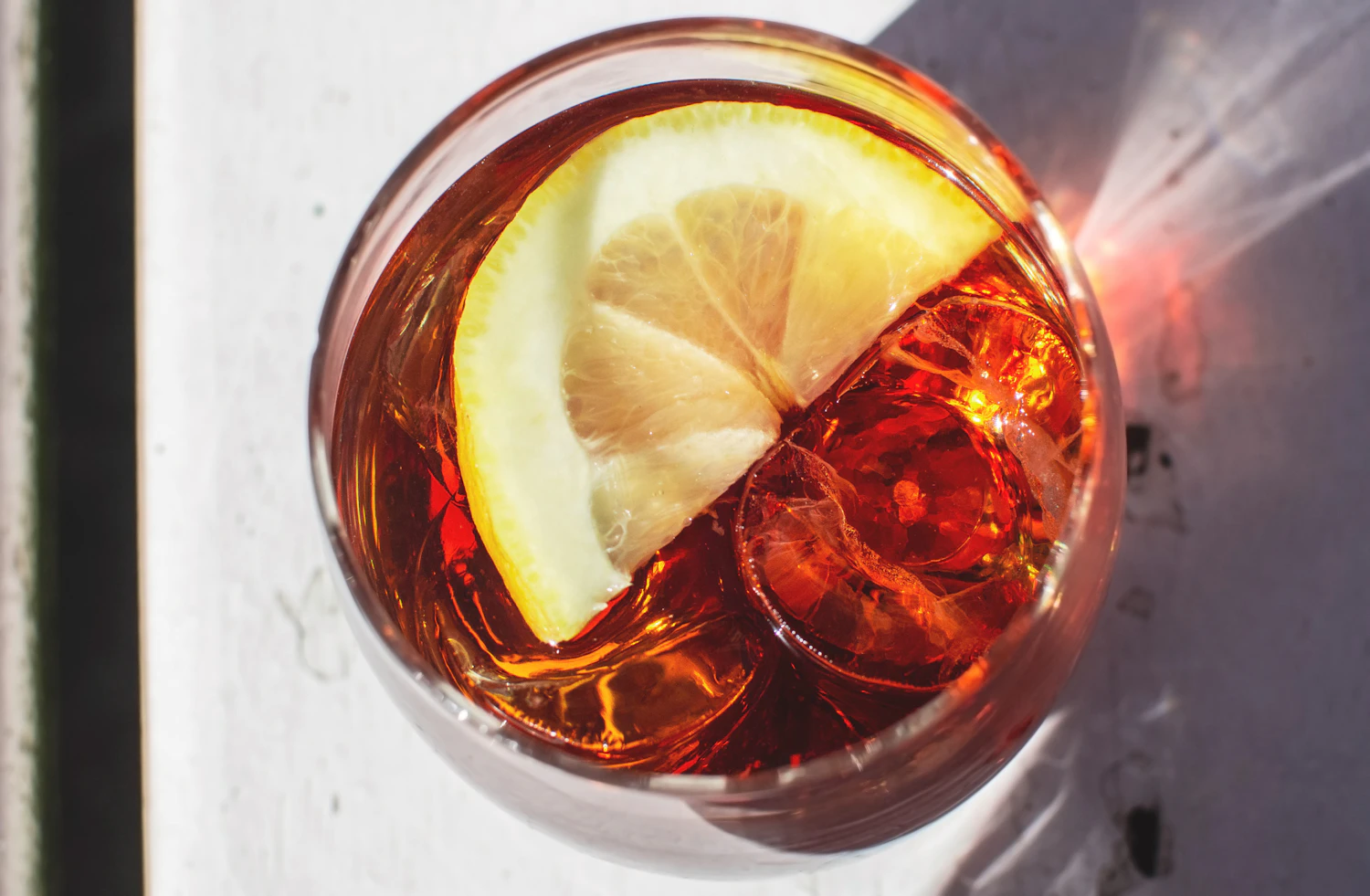 An amber aperitivo over ice with a slice of lemon, seen from above in strong sunlight