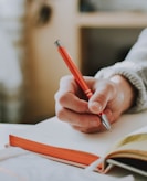 person holding on red pen while writing on book