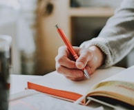 person holding on red pen while writing on book