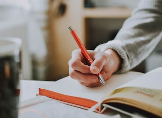 person holding on red pen while writing on book