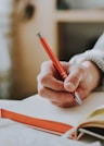 person holding on red pen while writing on book