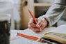 person holding on red pen while writing on book